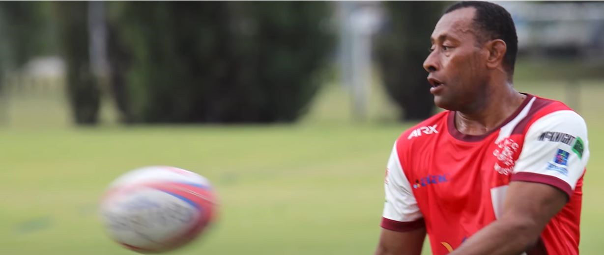 A Fijian Pacific labour mobility worker wearing a red and white shirt catches a football.
