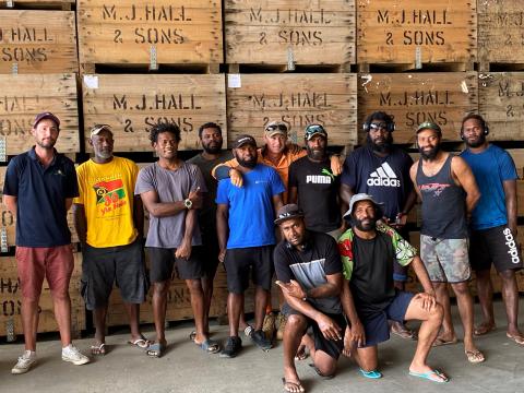 A group of Pacific Island men stand in a fruit packing shed.