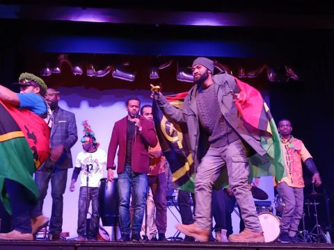 A man draped in a Vanuatu flag dances around a stage.