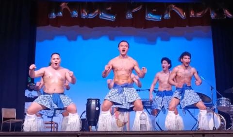 Samoan men wearing traditional costumes dance on stage.