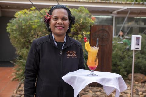 A waitress stands smiling holding a tray with a cocktail