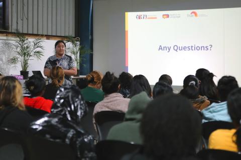 A woman standing beside a projector screen presenting to a group of people
