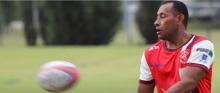 A Fijian Pacific labour mobility worker wearing a red and white shirt catches a football.