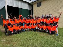A large group of PNG women in orange high-visibility workwear in front of a shed.