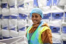 A PALM scheme worker wearing protective plastic cap and bib, a yellow reflective vest and a brown fleecy hoodie smiles at the camera.