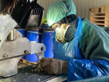 A person sits at a machine wearing PPE