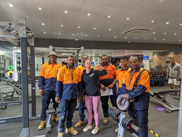 Fijian men in orange hi-vis uniforms stand in a gym