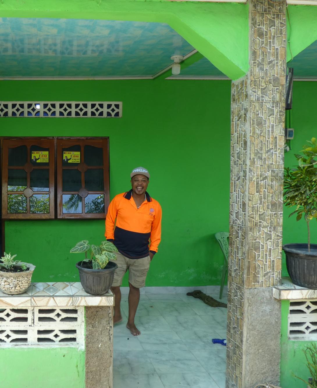 A man in high visibility shirt standing in front of a green house.