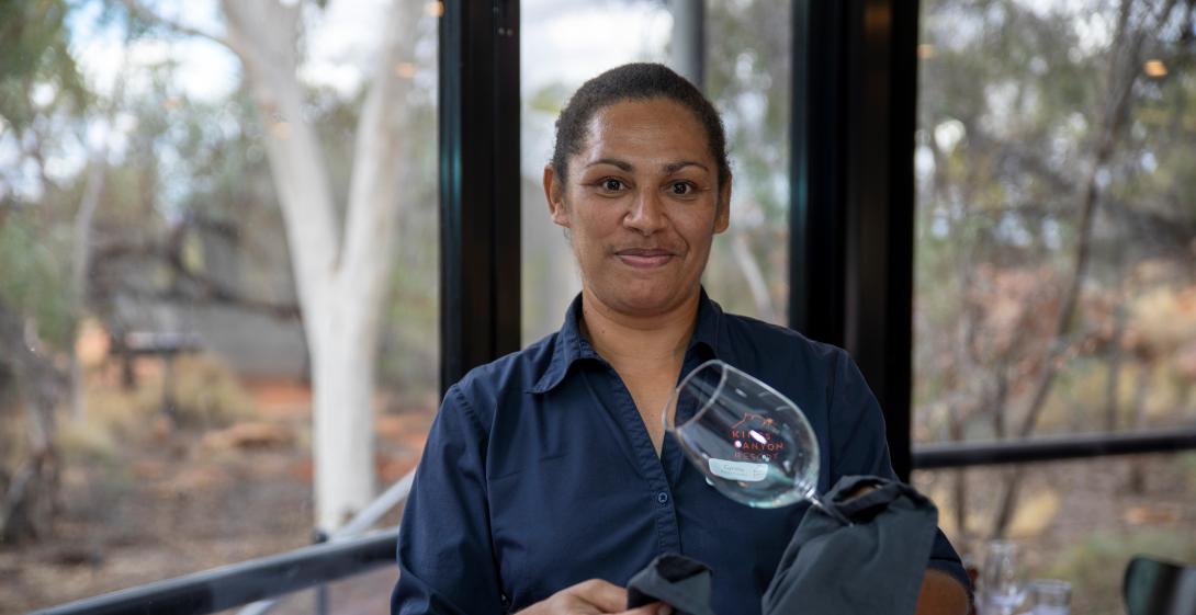 A woman standing in a restaurant cleaning a wine glass