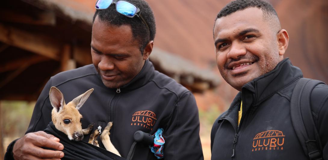 Two men at Uluru, one of them holding a joey 